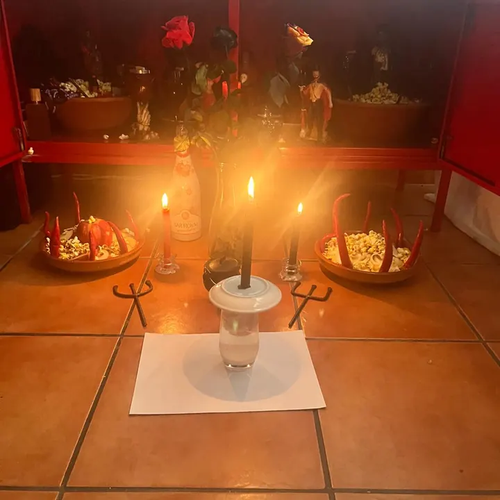 Altar vermelho com velas, oferendas e imagens, preparado para trabalho